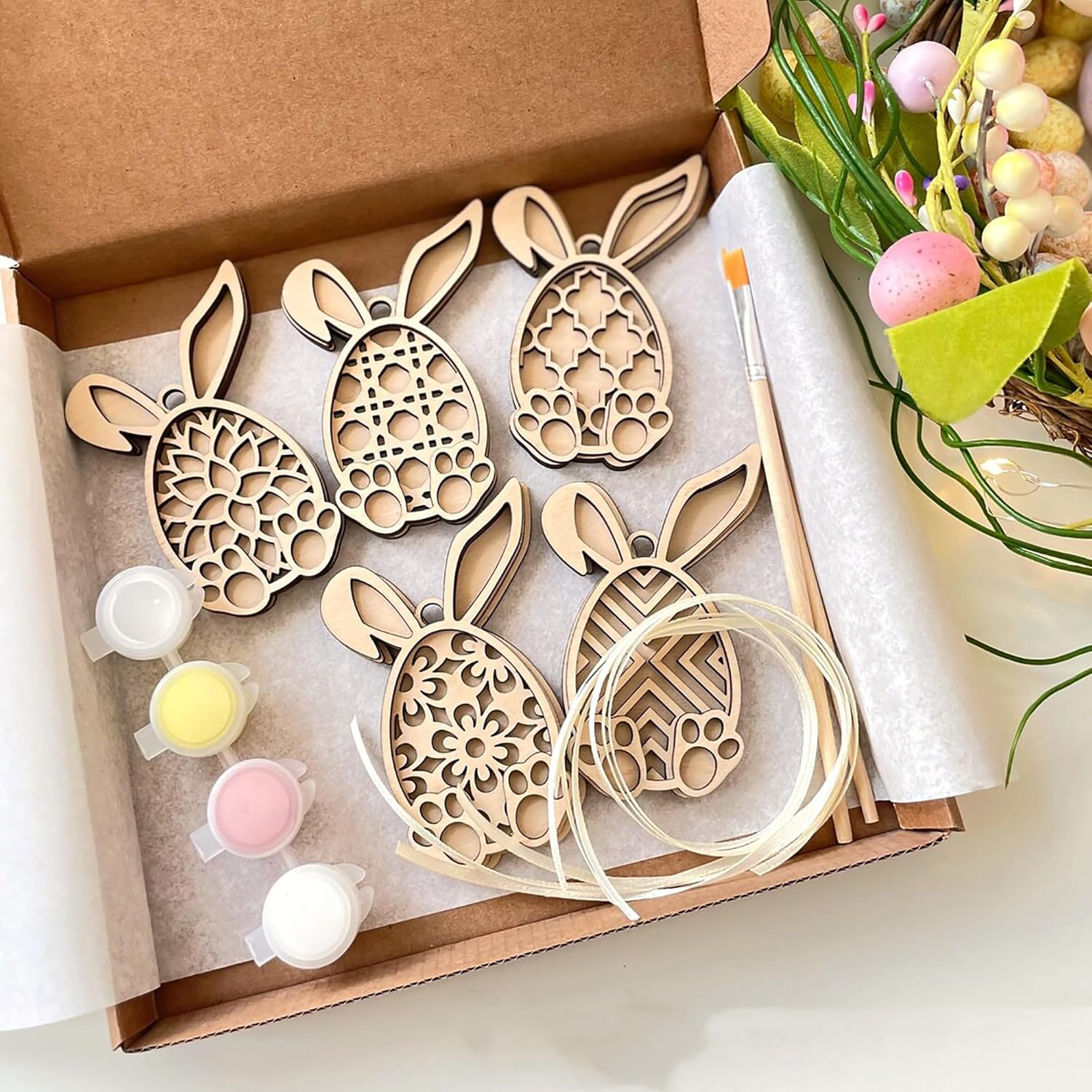 Wooden Easter bunny and egg ornaments in a box with paint supplies.
