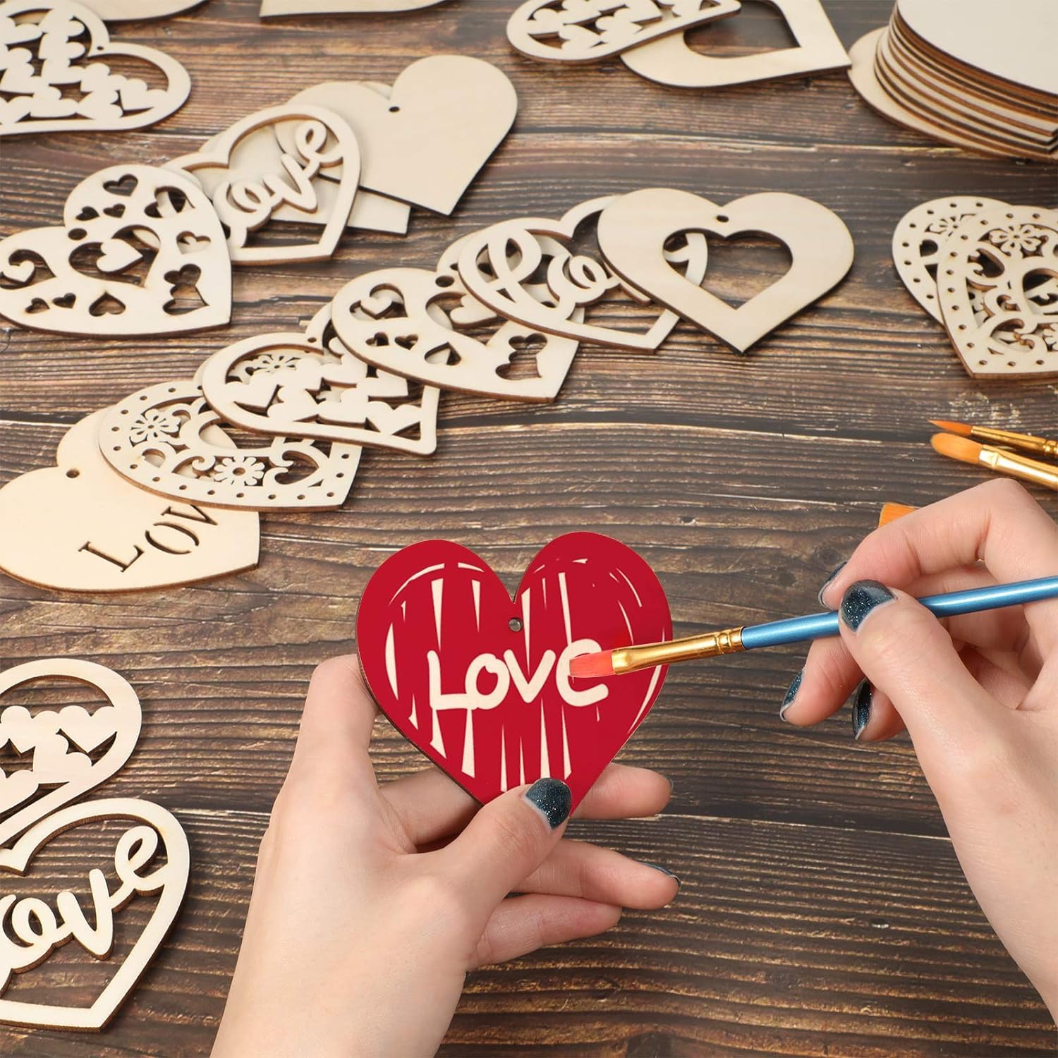 Person painting a red heart-shaped wooden cutout with 'love' on a wooden table.