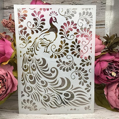 Decorative card with peacock design surrounded by pink flowers on a wooden surface
