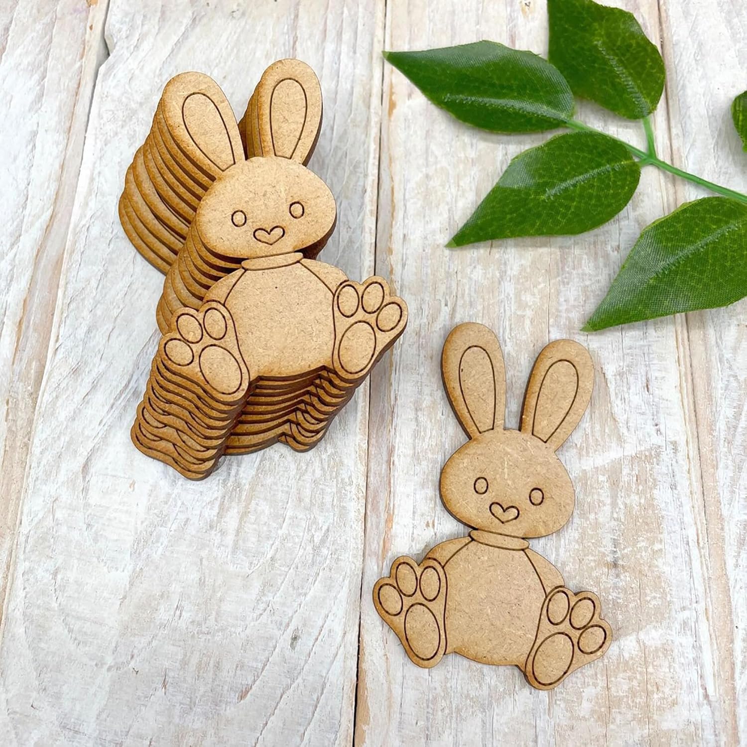 Stack of wooden bunny shapes on a light wooden surface with green leaves.