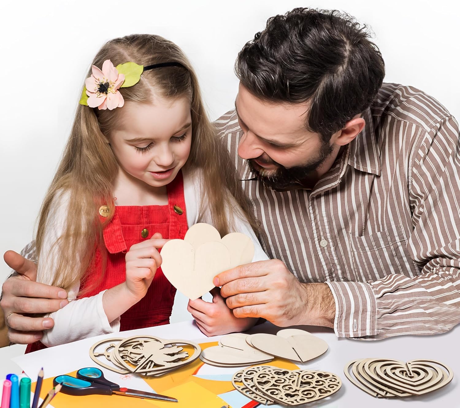 Man and young girl crafting wooden heart shapes together on a table.