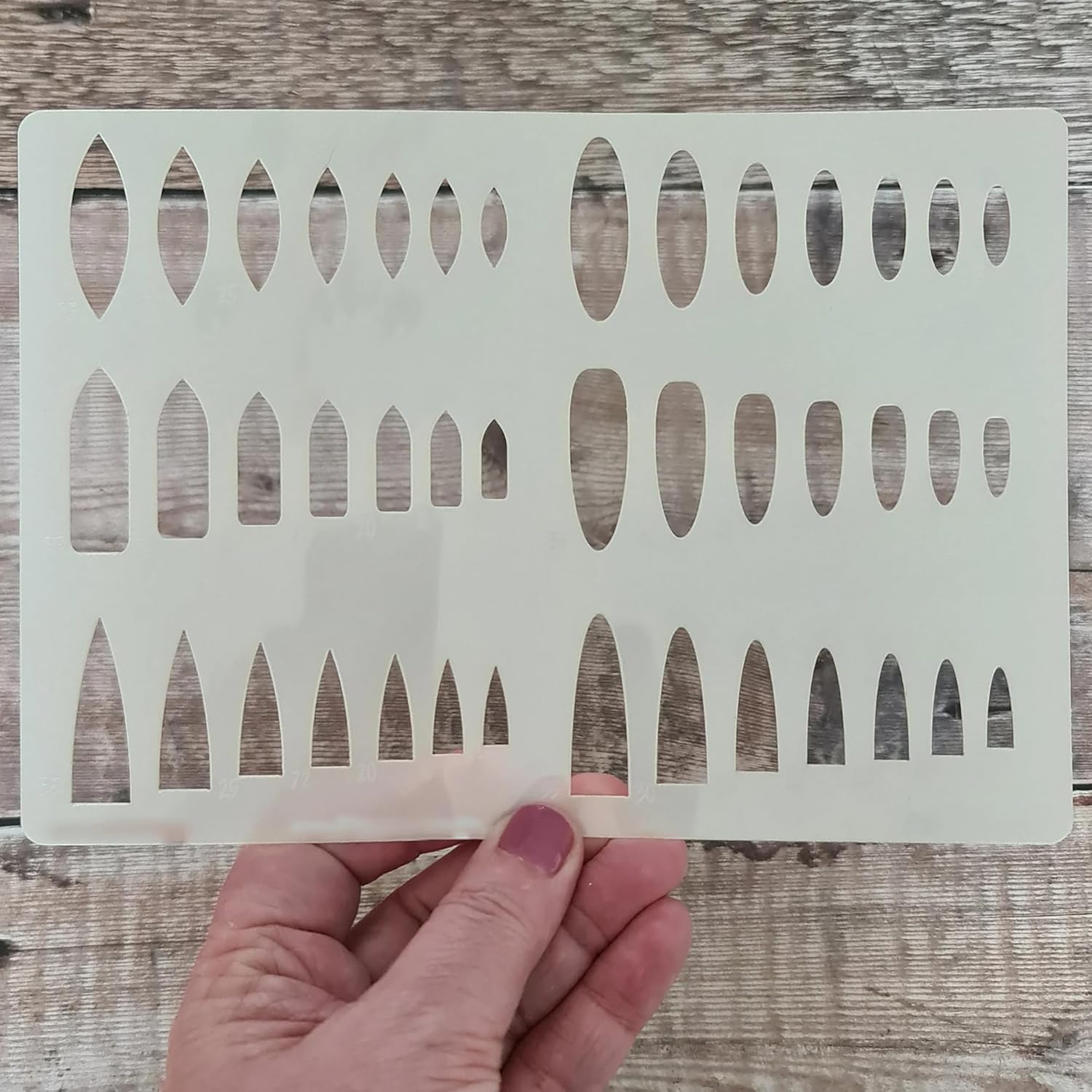 Hand holding a white stenciling template with geometric cutouts on a wooden surface