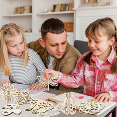 Man and two young girls working on a craft project with wooden cutouts in a home setting.
