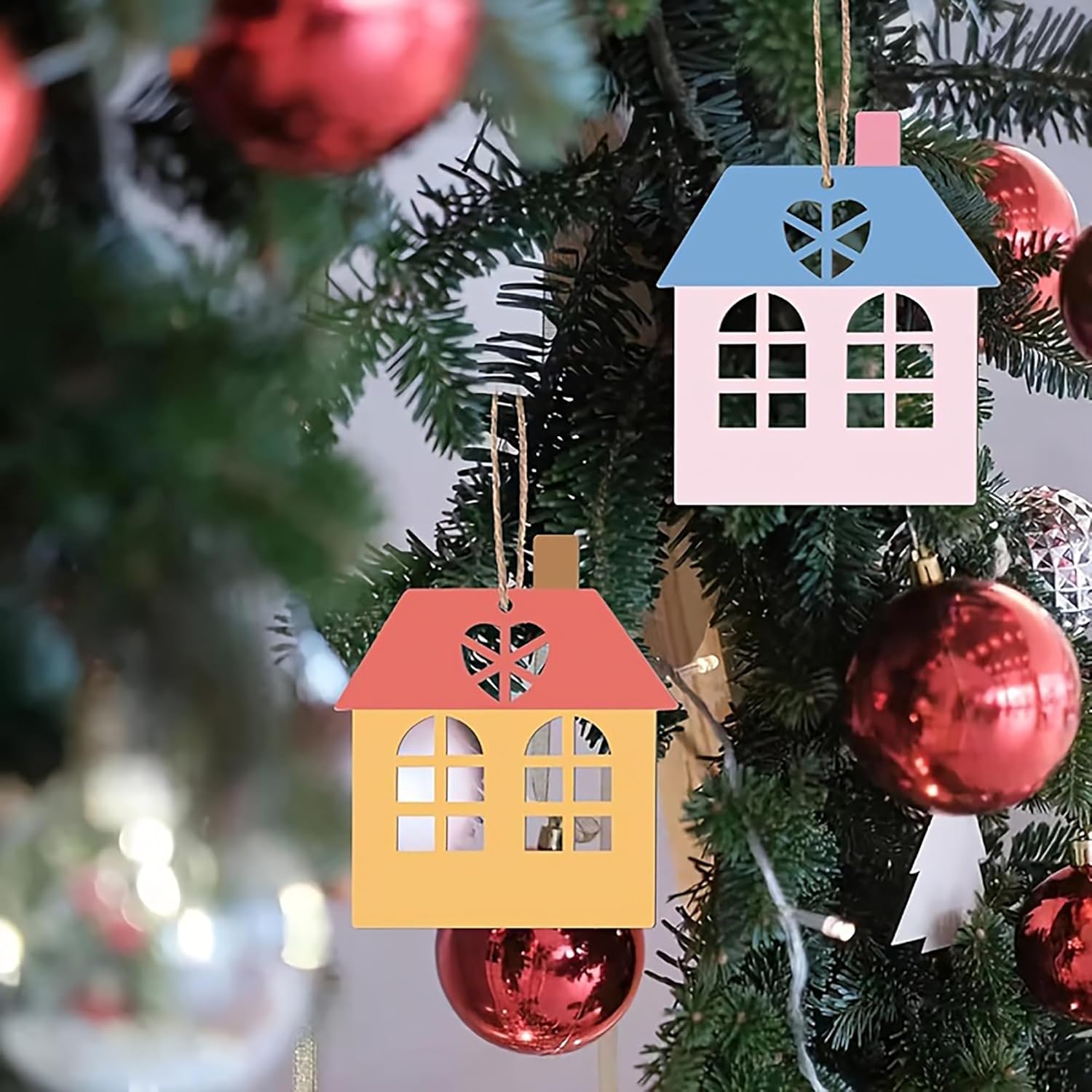 House-shaped Christmas ornaments on a tree with red baubles