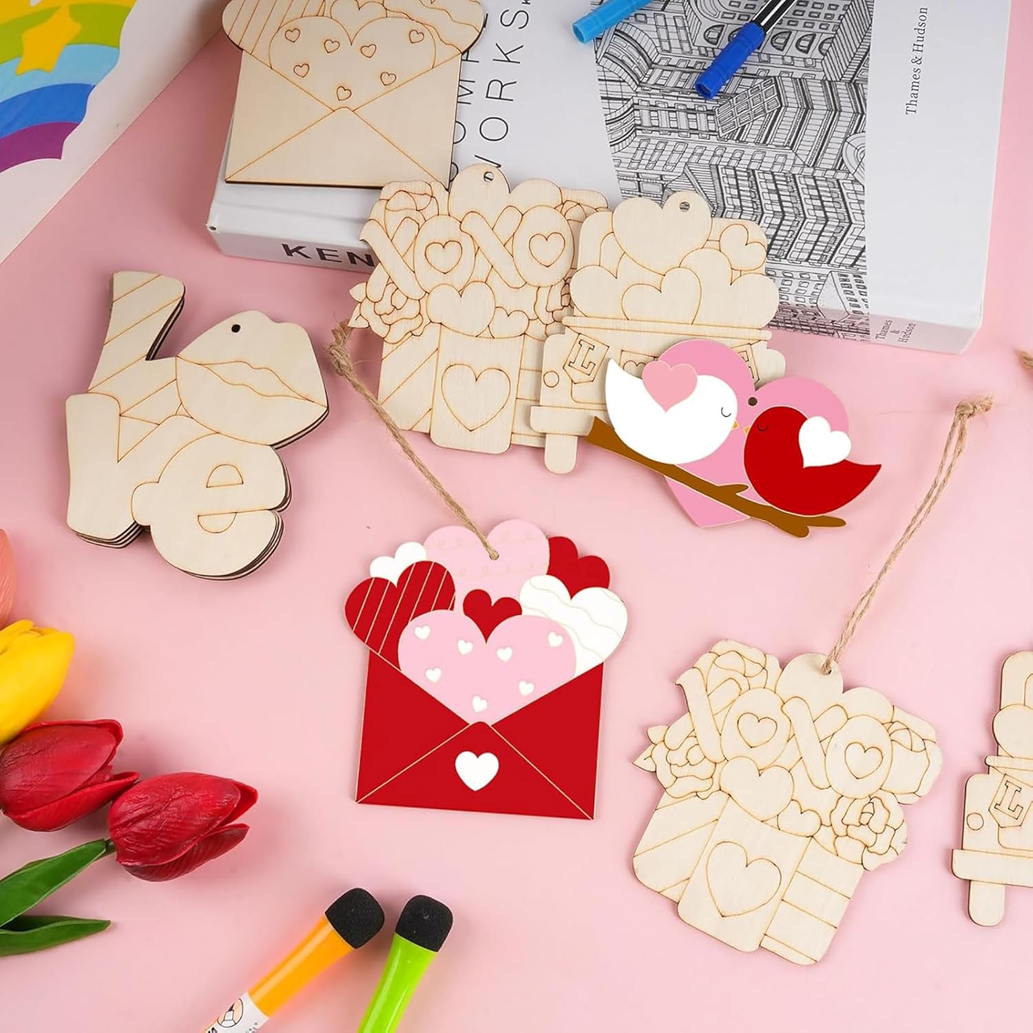 Wooden heart-shaped decorations on a pink surface with markers and tulips.