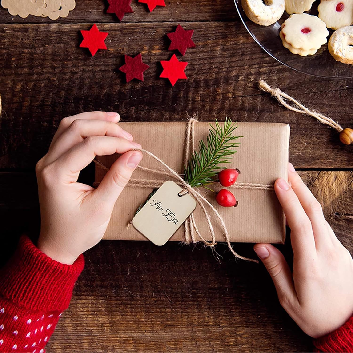Person wrapping a gift with a small tree branch and red berries on a wooden surface.