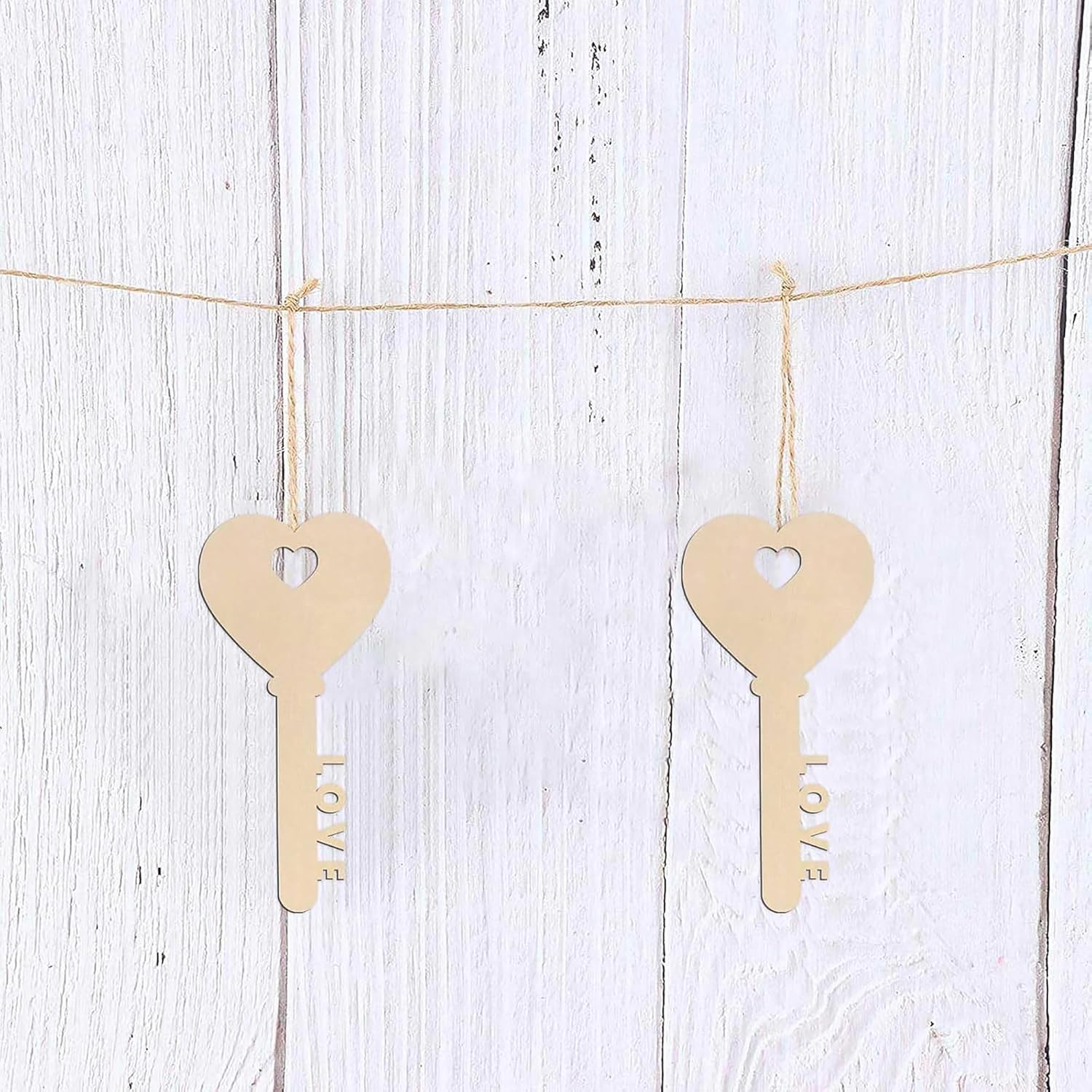 Two wooden key-shaped cutouts with 'LOVE' engraved on them, hanging on a string against a white wooden background.