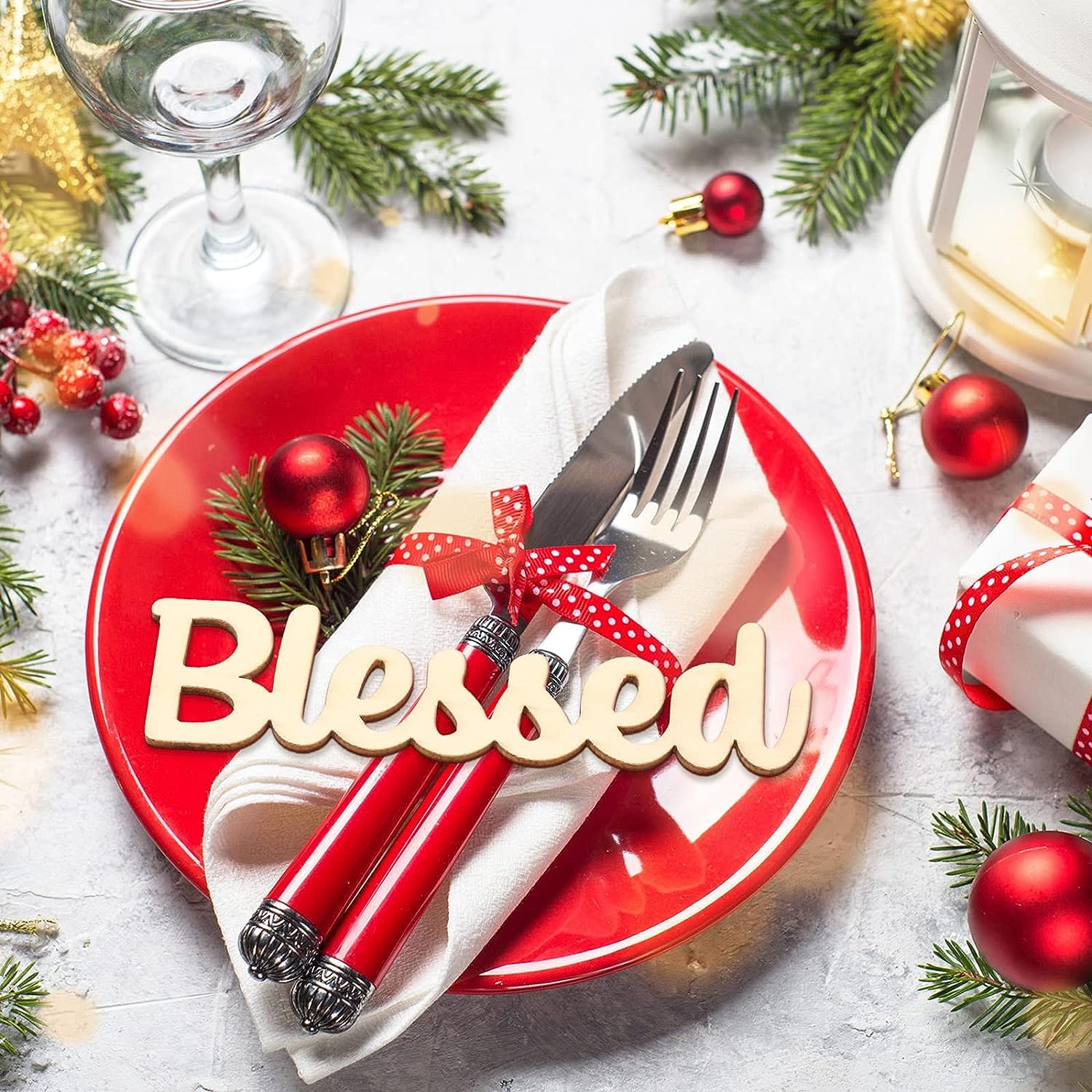 Christmas table setting with a red plate, silverware, and festive decorations on a white surface.