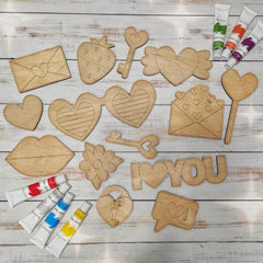 Wooden shapes with 'I love you' on a wooden surface with paint tubes.