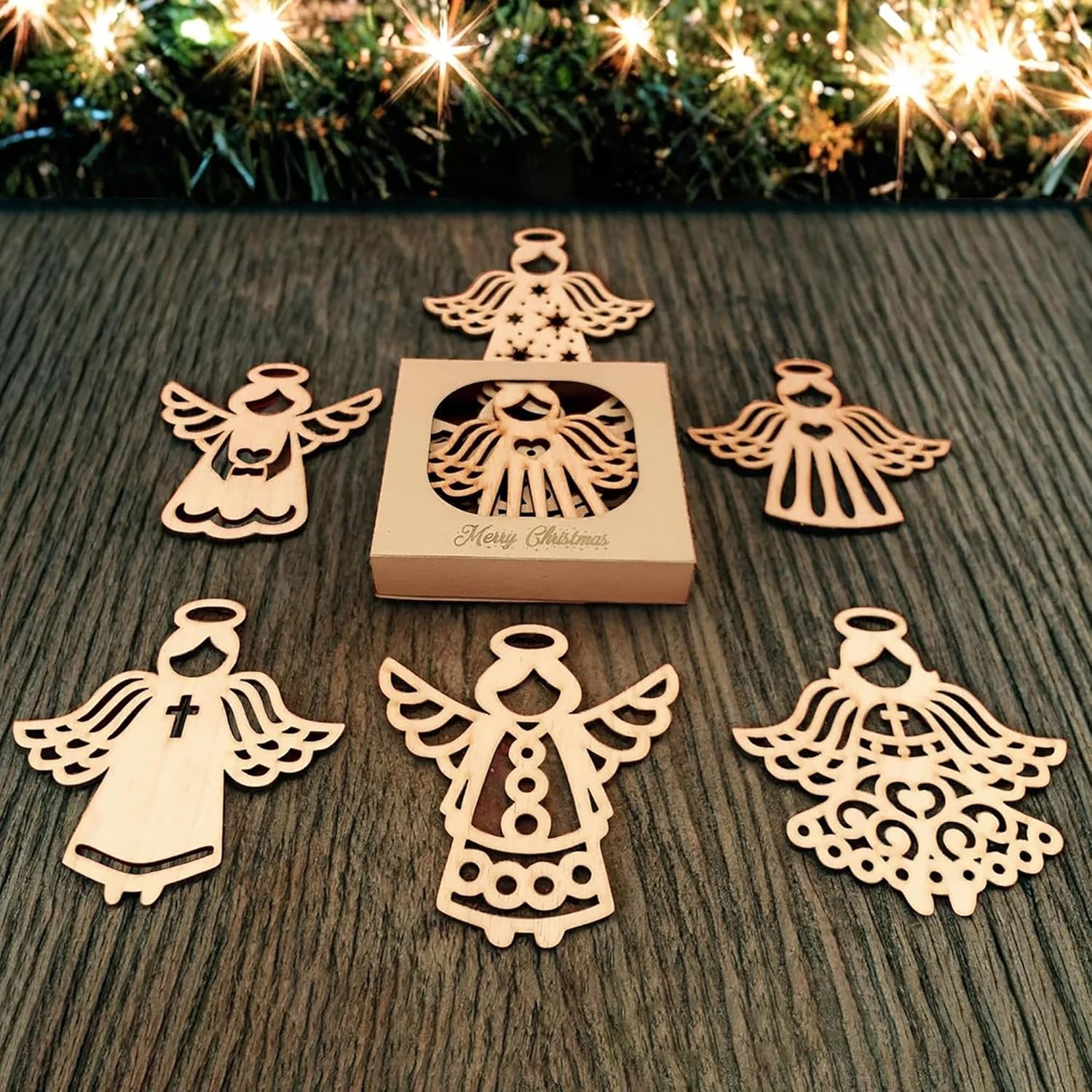 Wooden angel decorations with a box on a wooden surface, Christmas tree in the background