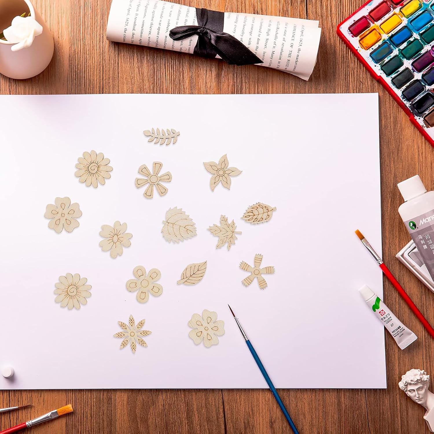 Art supplies including flowers, paintbrushes, and watercolor paints on a wooden table.