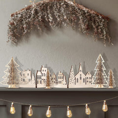 Decorative cityscape with trees and lights on a shelf against a gray wall.