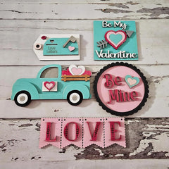 Valentine-themed decorative items including a truck, heart-shaped signs, and 'Love' banner on a wooden surface.