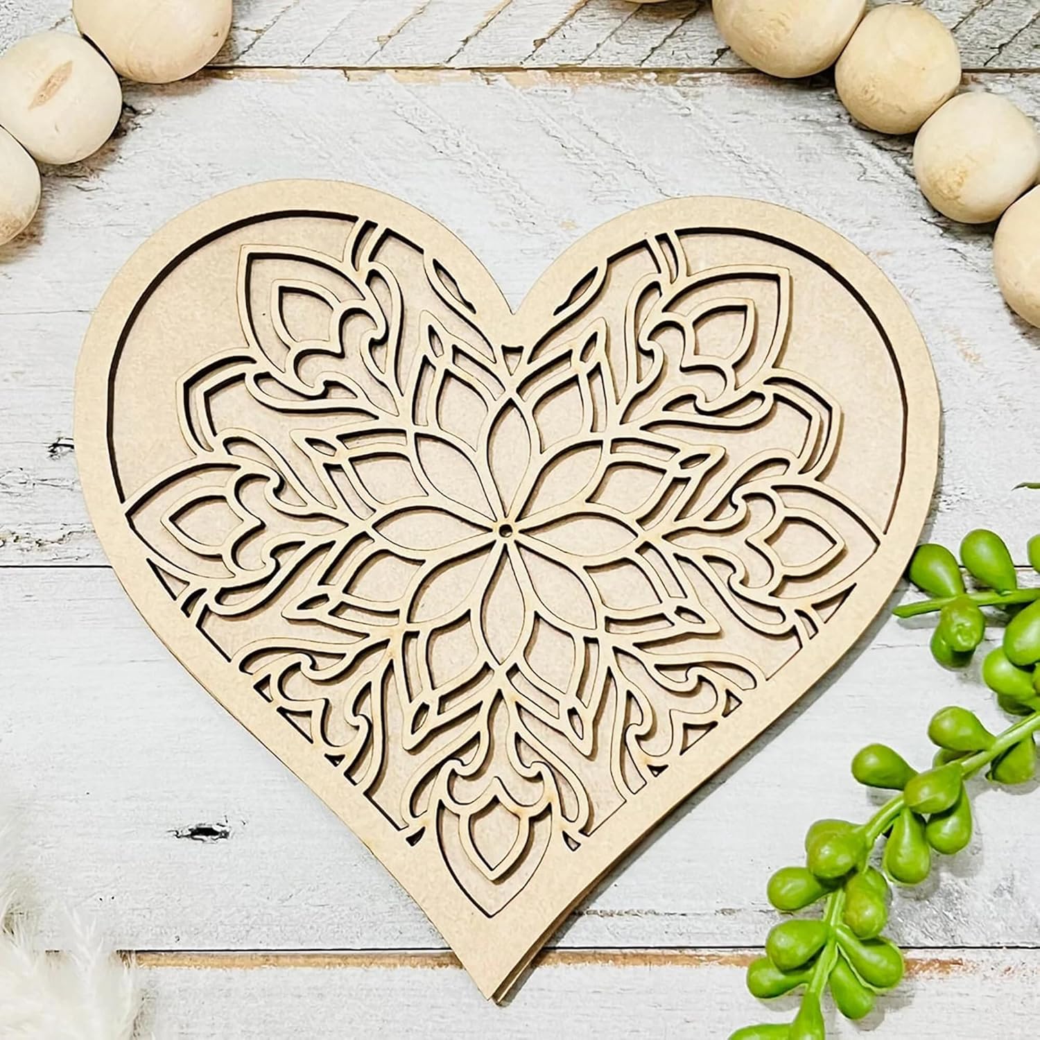 Wooden heart-shaped decorative item with intricate patterns on a wooden surface with beads and greenery.