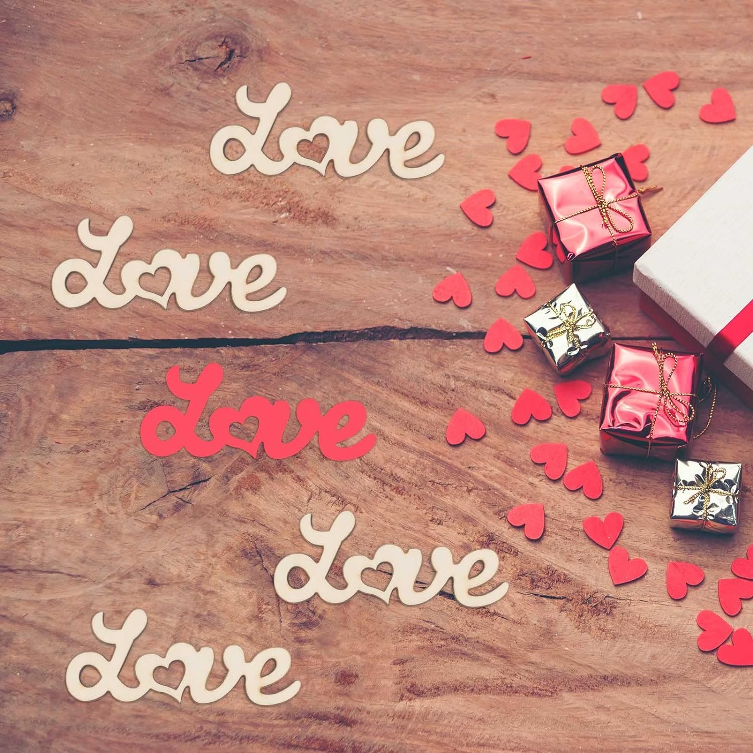 Wooden surface with 'love' word cutouts, small gift boxes, and red heart-shaped confetti.