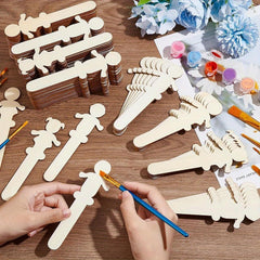 Wooden craft figures on a table with hands painting one of them, surrounded by art supplies.