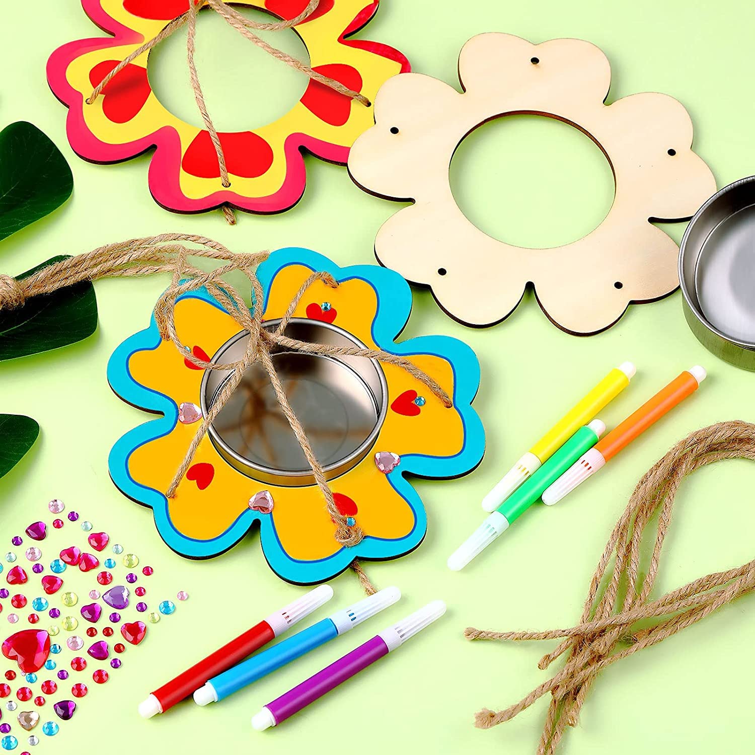 Colorful craft materials including flower-shaped frames, markers, beads, and string on a light green background.