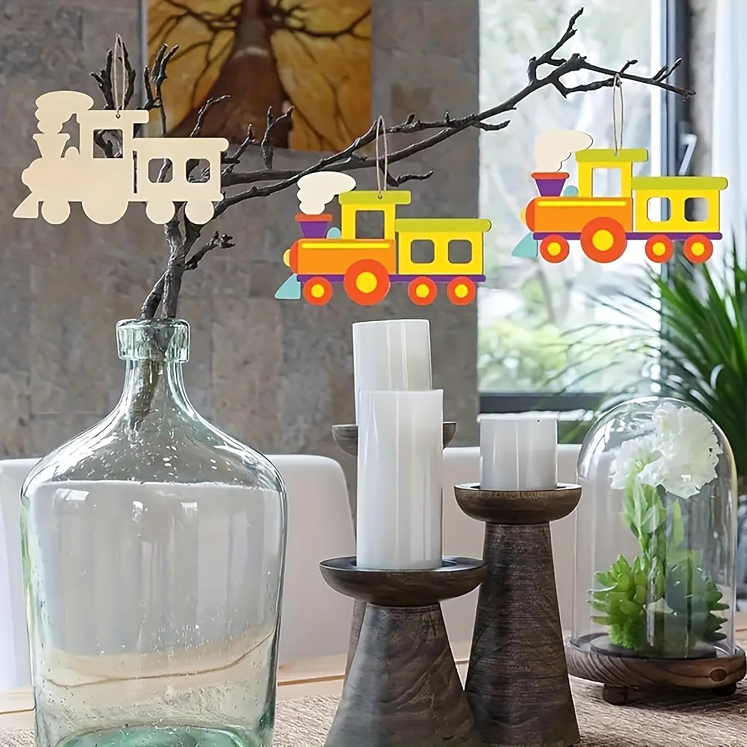 Decorative train ornaments on a branch with a glass vase and candles in the background.