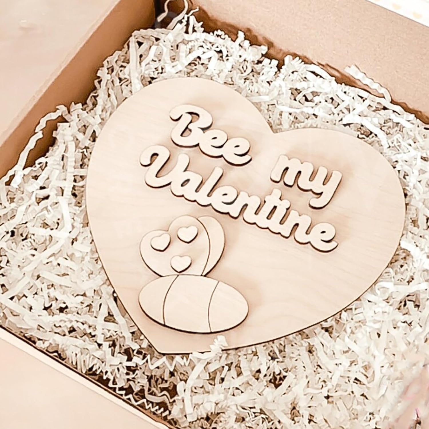 Heart-shaped wooden ornament with 'Bee my Valentine' text on a white shredded paper background