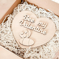 Heart-shaped wooden ornament with 'Bee my Valentine' text on a white shredded paper background