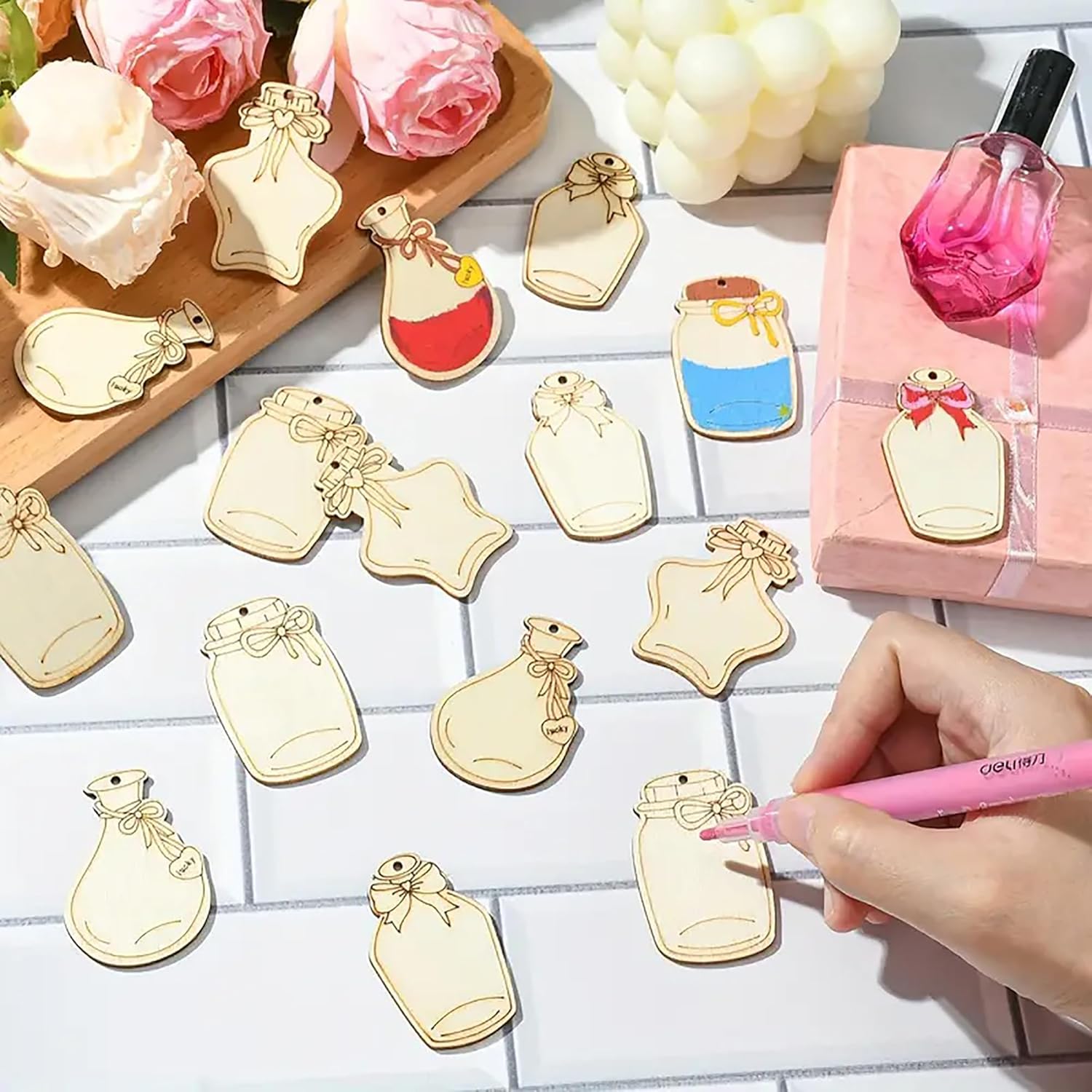 Decorative bottle-shaped charms on a table with a hand holding a pink pen.
