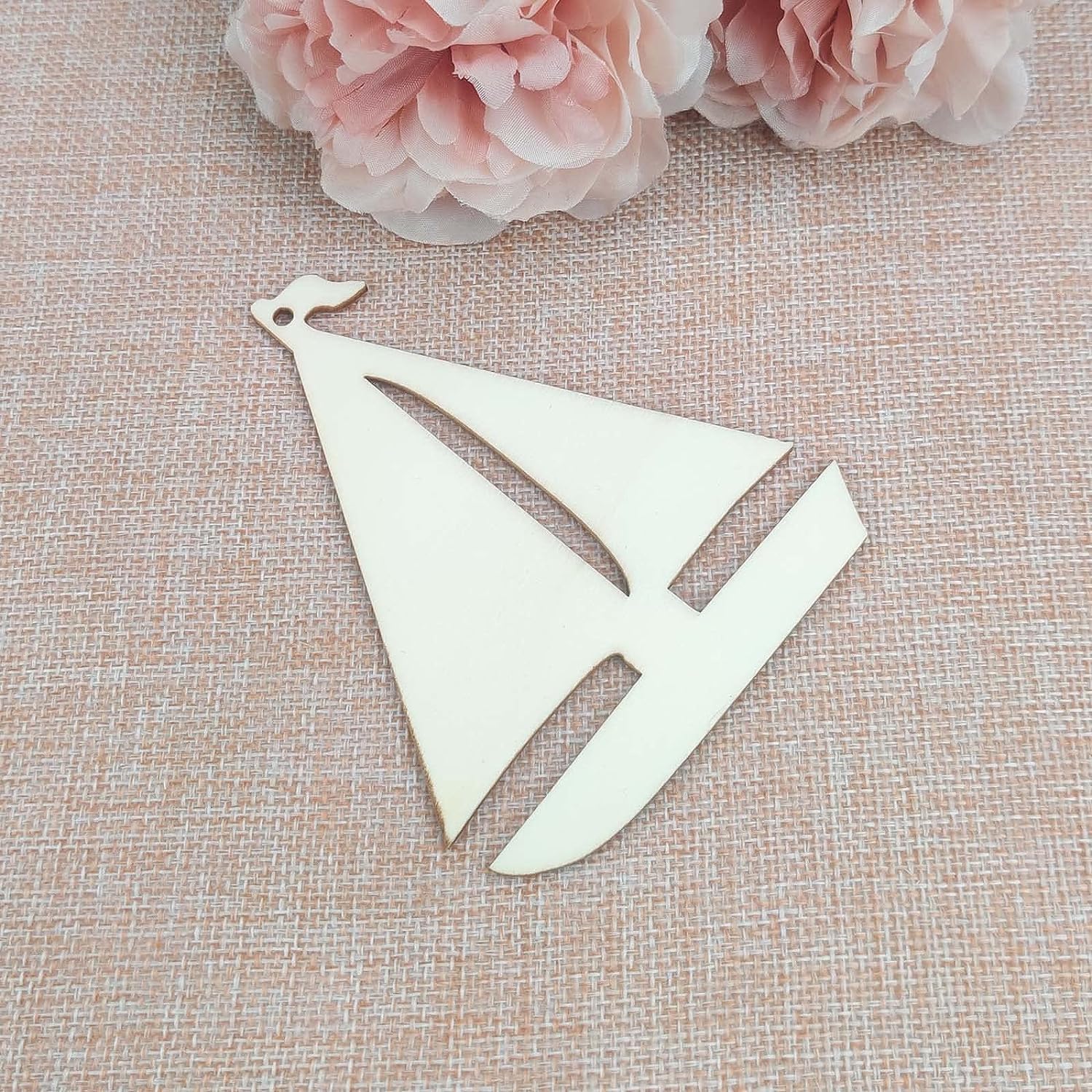 Metallic sailboat ornament on a textured beige surface with pink flowers in the background