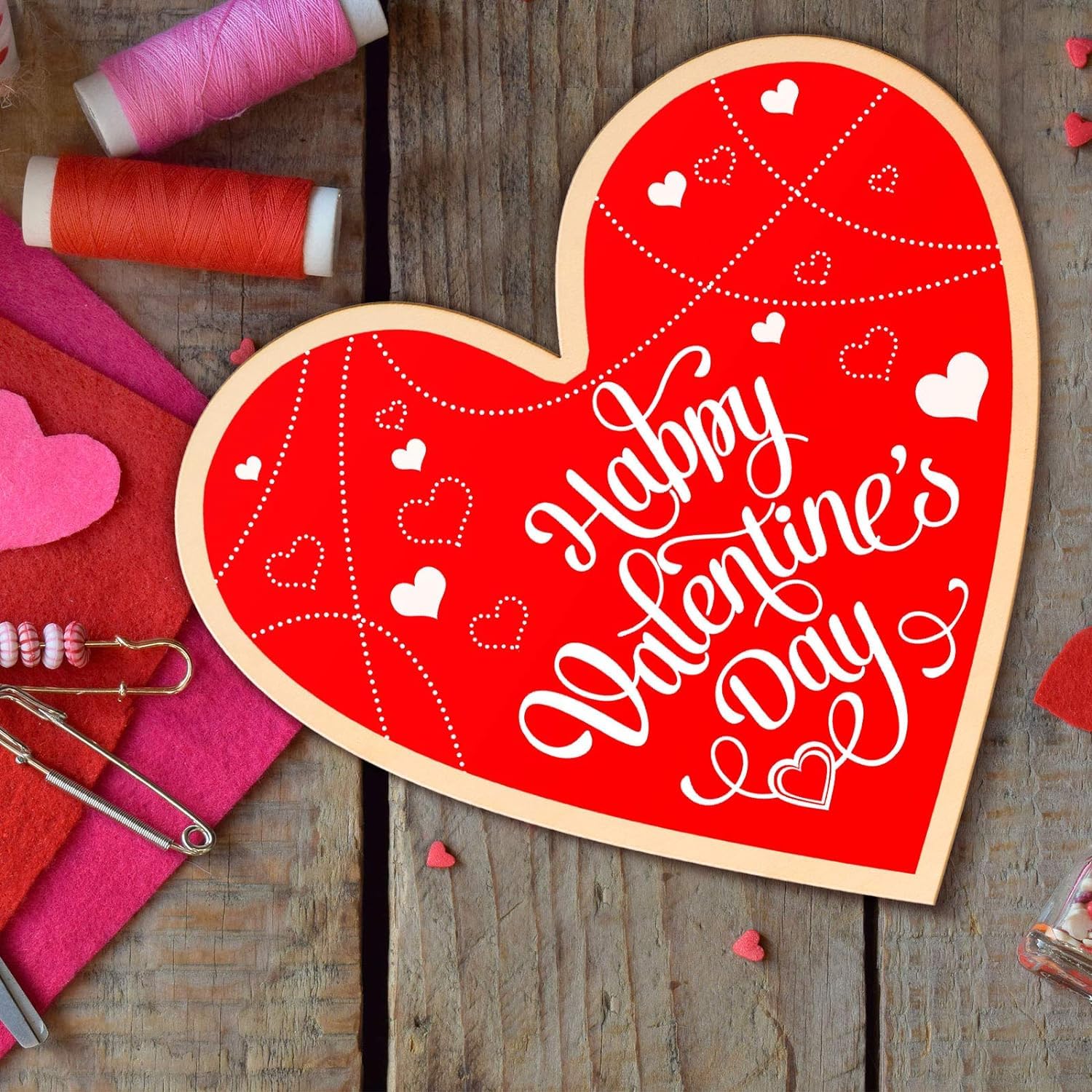 Heart-shaped wooden sign with 'Happy Valentine's Day' text on a wooden surface with sewing materials.