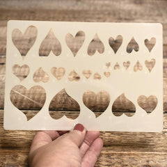 Heart-shaped stencil held by a hand on a wooden surface