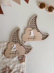 Wooden baby milestone signs shaped like a moon and a cloud with '2 months' and '1 month' text on a neutral background.