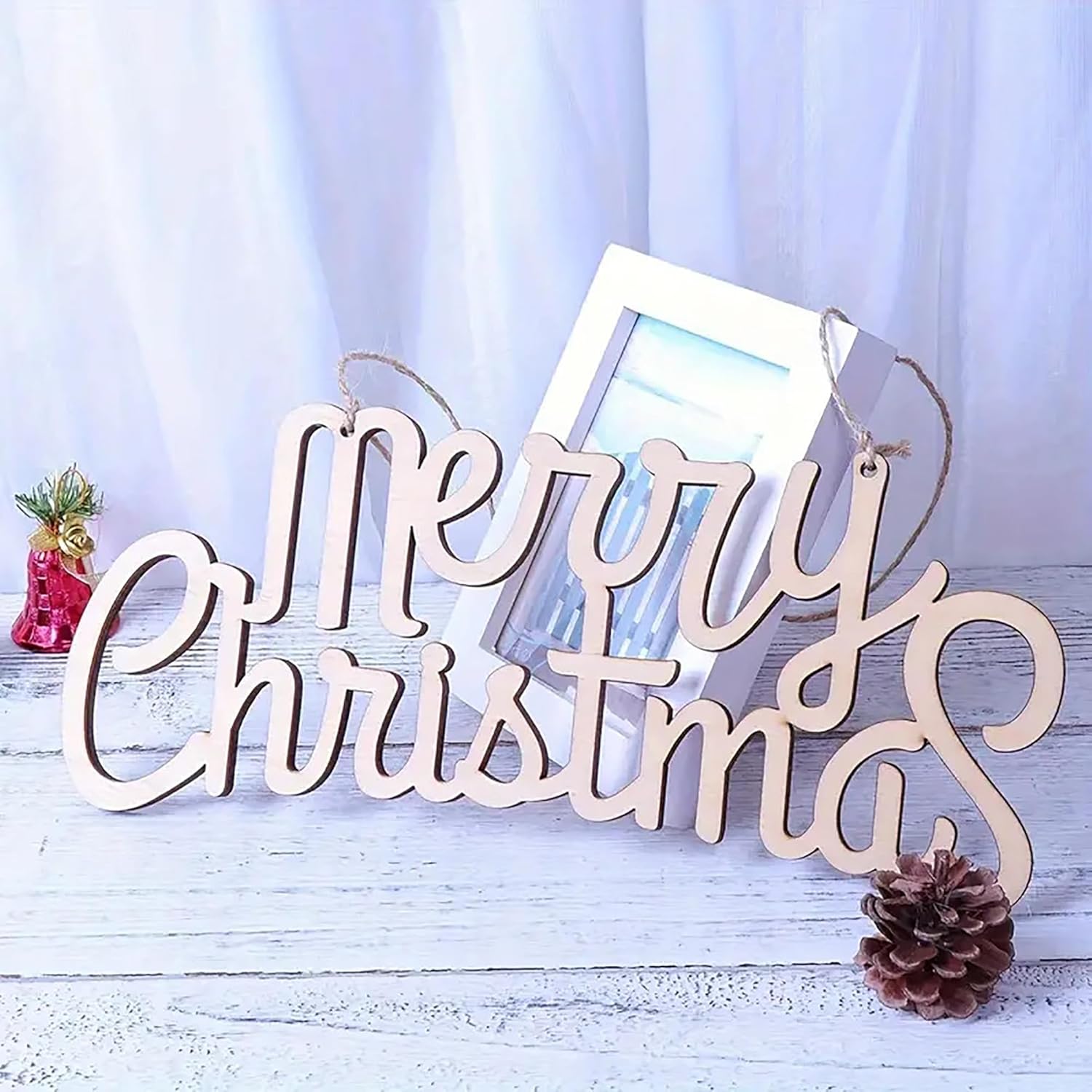 Wooden 'Merry Christmas' sign with a photo frame and pine cone on a light blue background