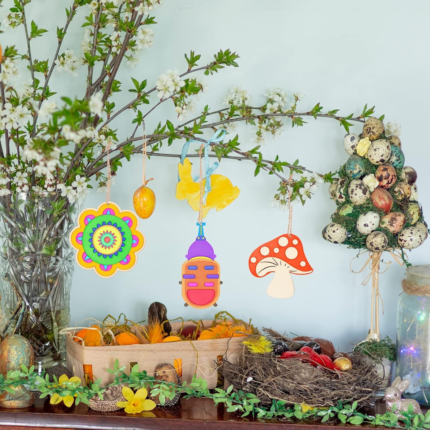 Decorative setup with Easter eggs, flowers, and a wreath on a light blue wall.
