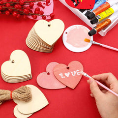 Heart-shaped wooden tags being painted with 'LOVE' on a red surface, surrounded by paint supplies.