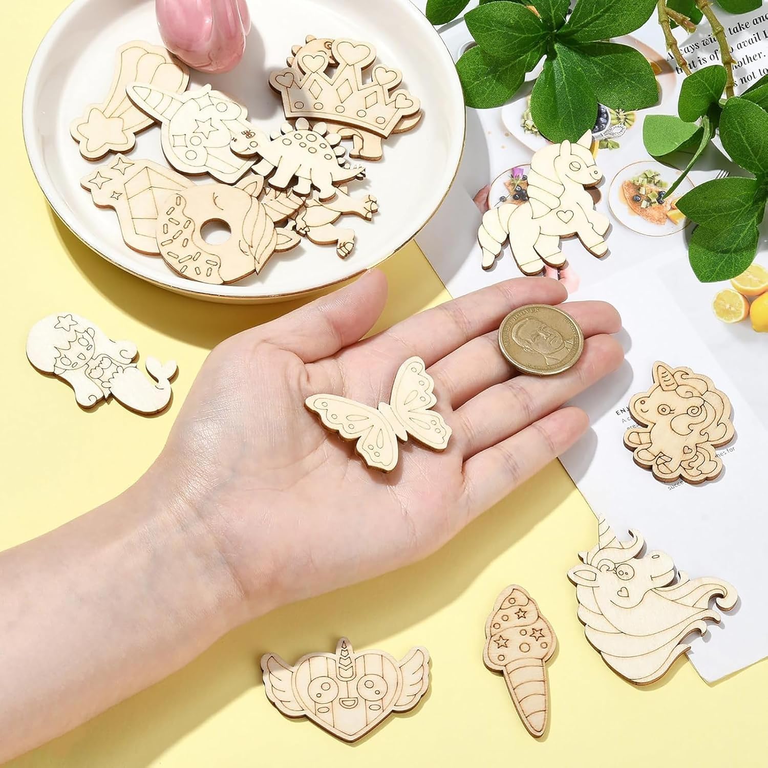 Wooden decorative pieces on a yellow surface with a hand holding a butterfly piece.