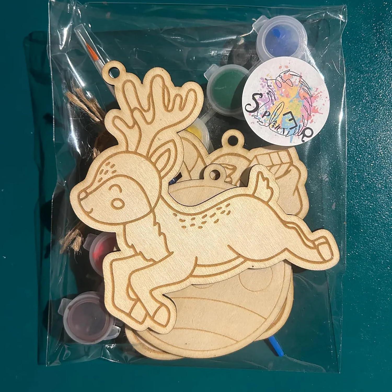 Wooden craft kit with animal shapes and paint bottles in a clear bag on a teal background
