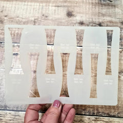 Transparent face mask with cut-out designs held by a hand on a wooden surface