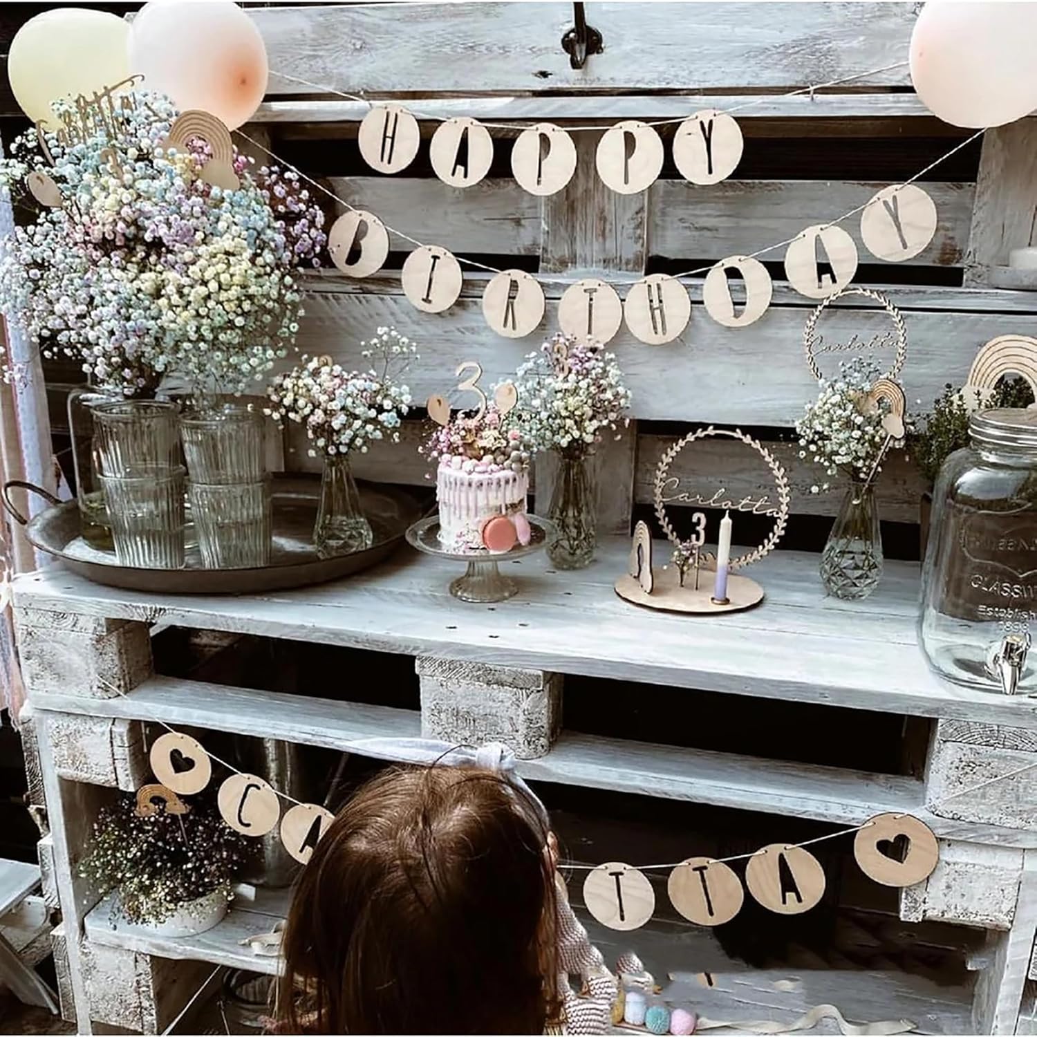 Decorative setup with flowers, a cake, and 'Happy Birthday' banner on a rustic wooden shelf.