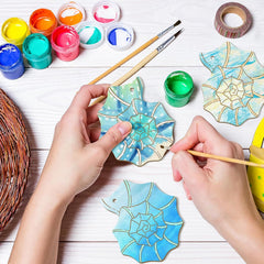 Hands painting decorative wooden pieces with colorful paint and tools on a white surface.