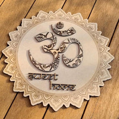 Decorative wooden sign with 'om' symbol and 'sweet home' text on a wooden surface