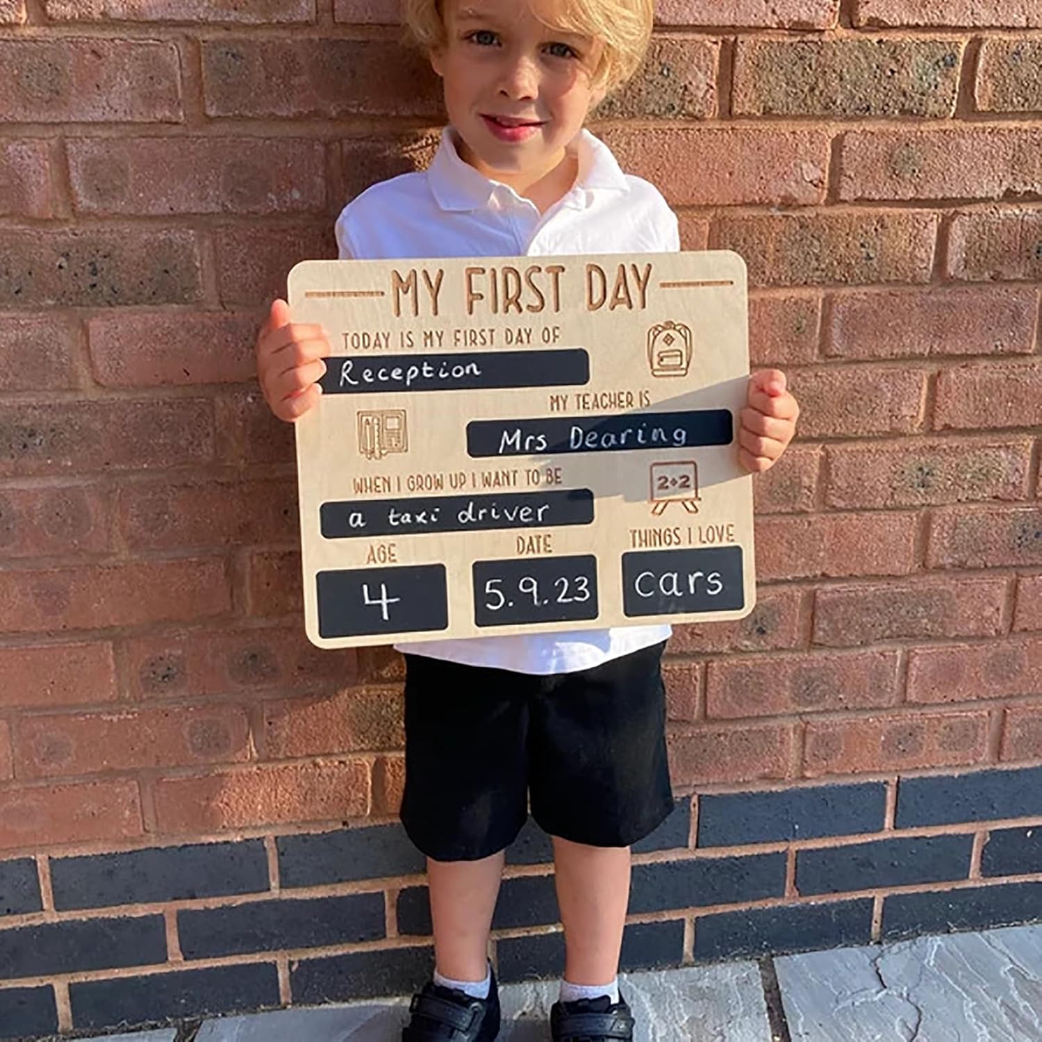 Child holding a sign for their first day of school in front of a brick wall.