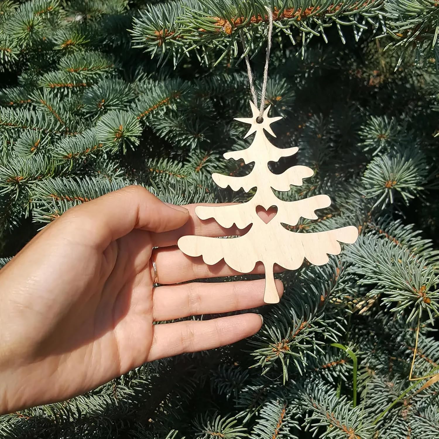 Wooden Christmas tree ornament held in front of a pine tree