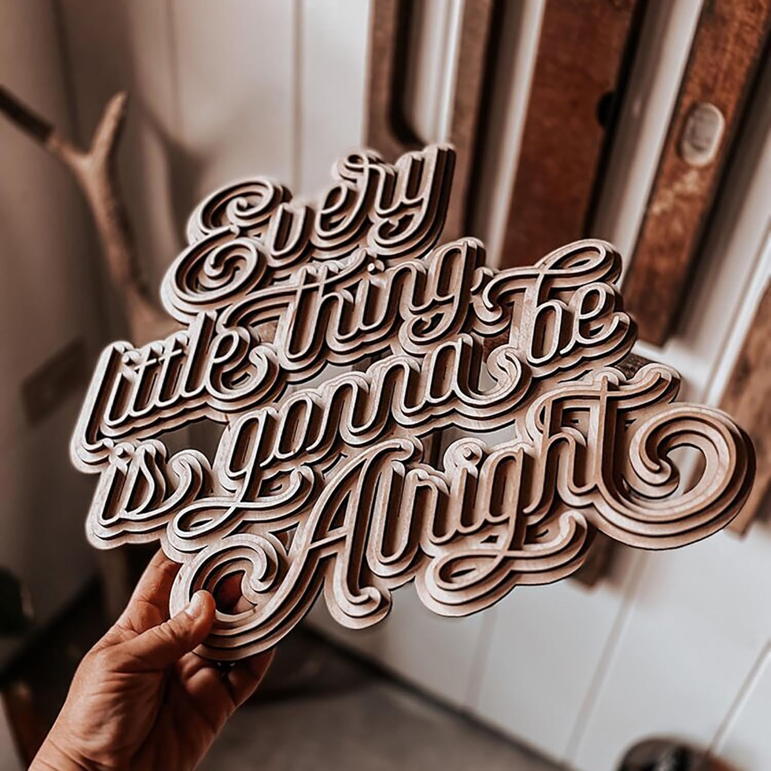 Wooden sign with 'Every little thing is gonna be alright' text held by a hand.
