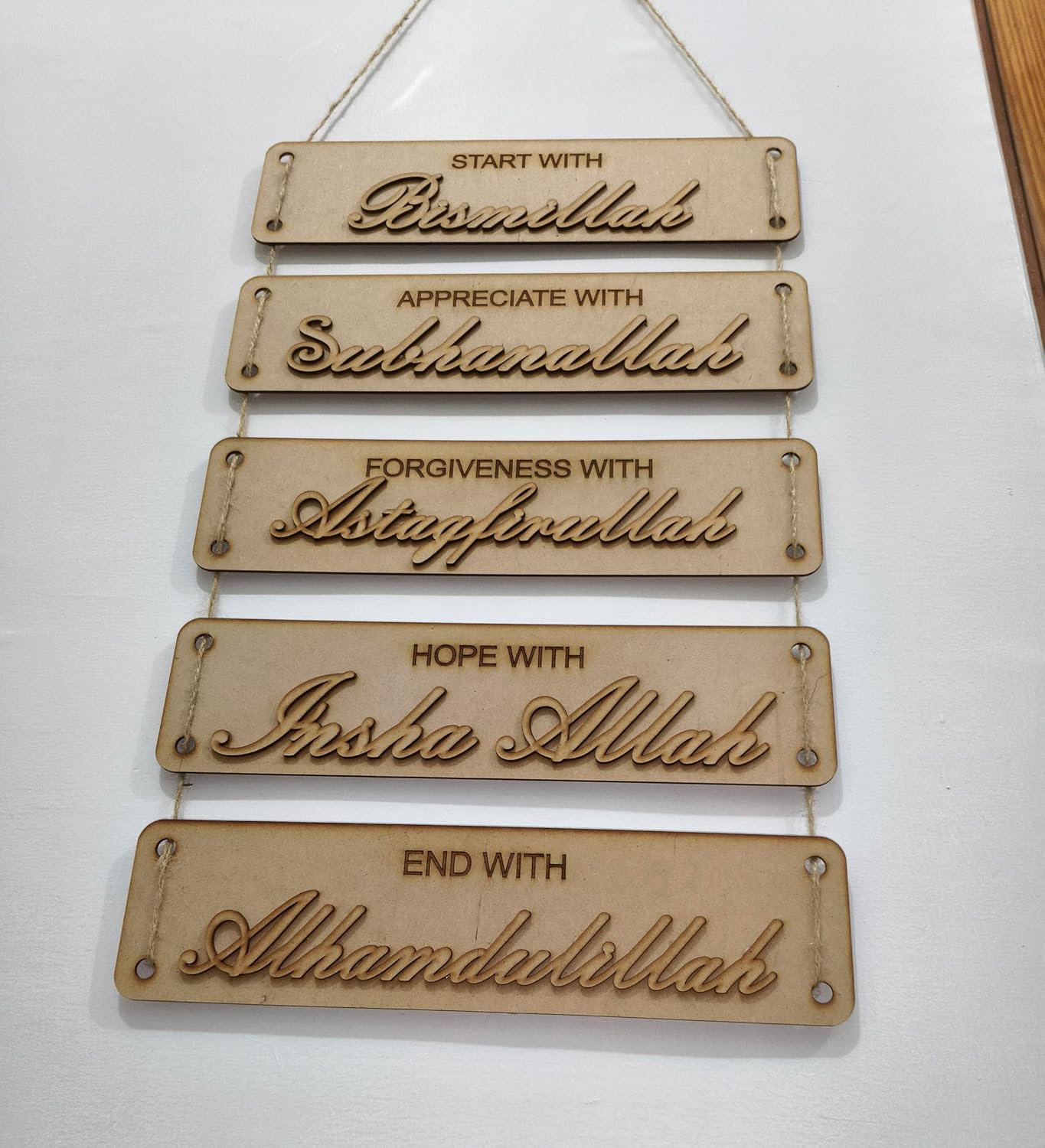Wooden wall hanging with engraved phrases on a white background