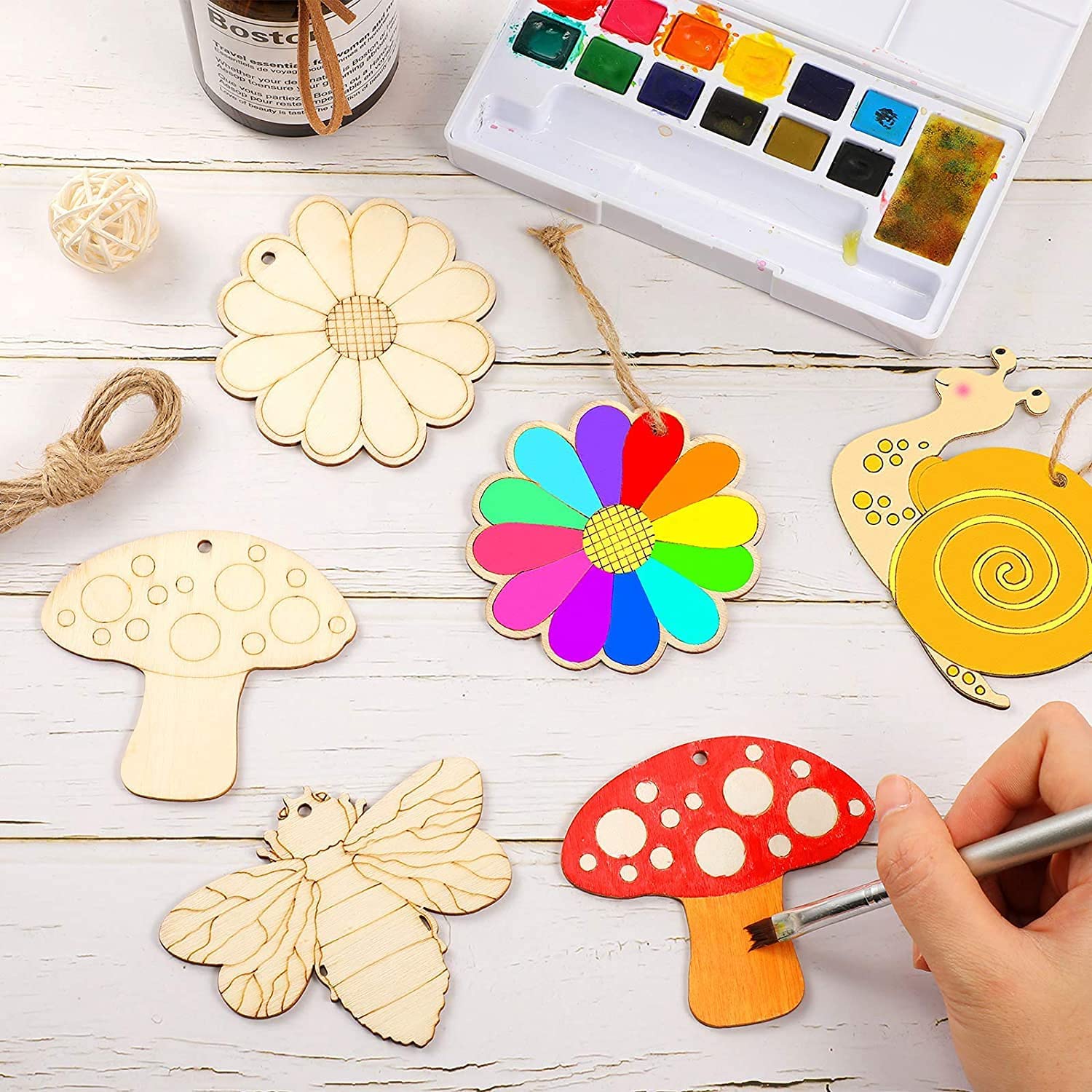 Colorful wooden ornaments being painted with a watercolor set on a wooden surface.