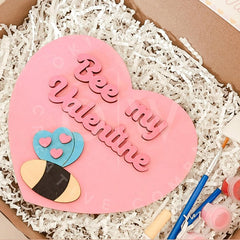 Pink heart-shaped cookie with 'Be my Valentine' text on a white crinkle paper background