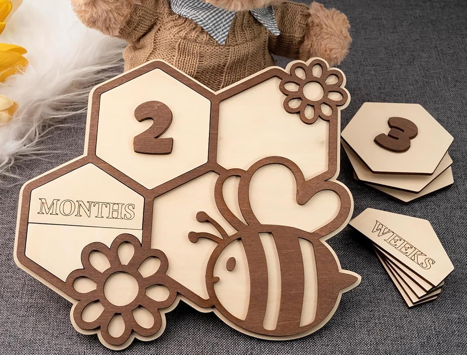 Wooden baby milestone card with bee design and small wooden cards on a textured surface.