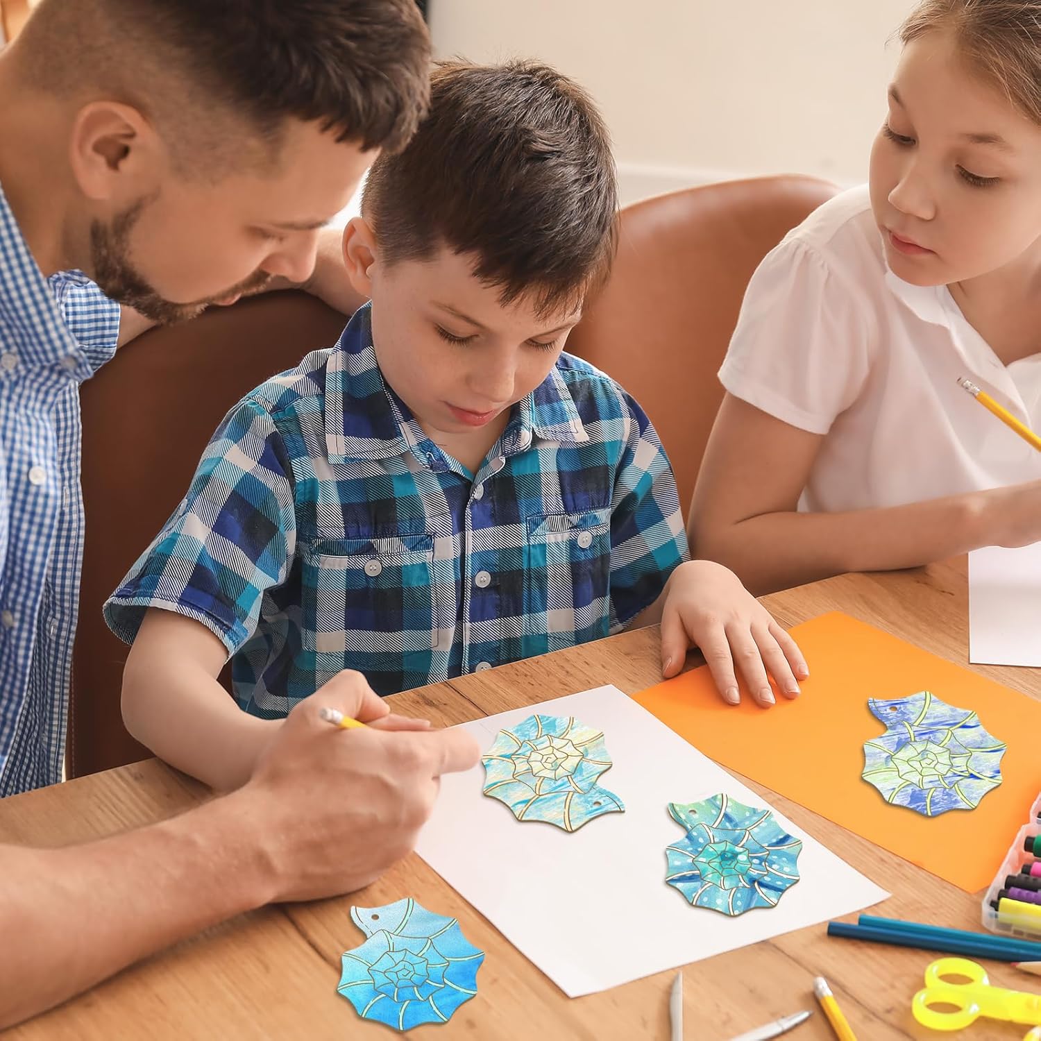 Man and two children working on a craft project at a table with colorful paper cutouts.