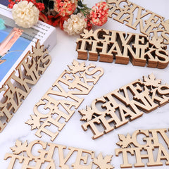 Wooden 'Give Thanks' decorations on a white surface with flowers in the background.