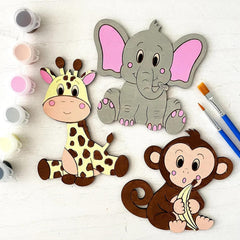Wooden animal cutouts (elephant, giraffe, monkey) with painting supplies on a light surface.