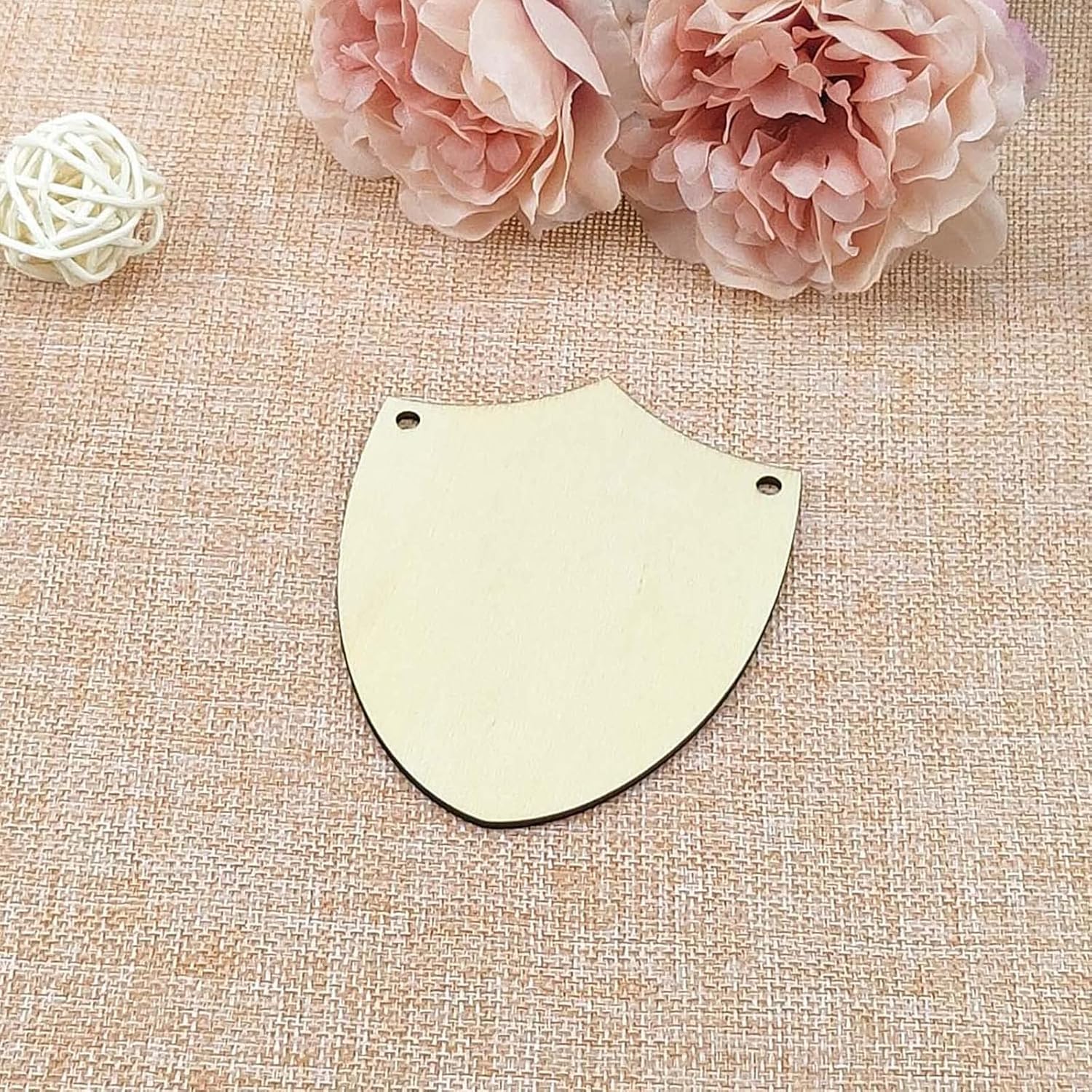 Shield-shaped gold pendant on a textured beige surface with pink flowers and a white decorative ball.