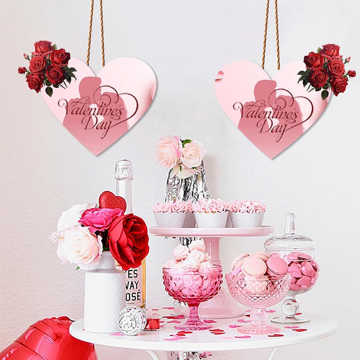 Valentine's Day-themed decor with heart-shaped signs, flowers, and sweets on a table.